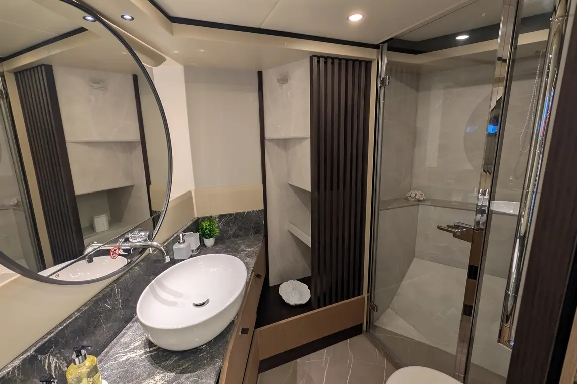 Modern bathroom featuring a round mirror, sink, shower enclosure, and stylish décor with grey tones and wooden accents.